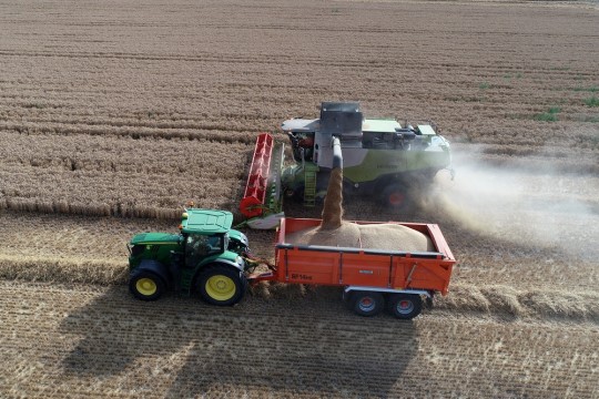 Imagem de colhetadeira despejando grãos na carroça aglobada em um trator agrícola