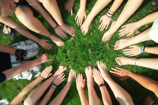 Imagem de um grupo de jovens reunidos em círculo com os pés e mãos juntados