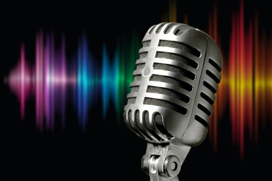 Imagem de um microfone prata metal e onda sonoras coloridas ao fundo