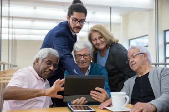 Imagem de idosos visualizando um tablet com ajuda de um jovem