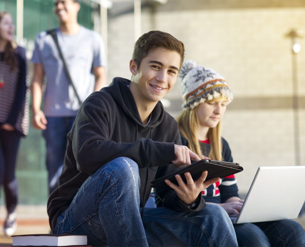Imagem de jovens com tablet e notebook nas mãos em um colégio